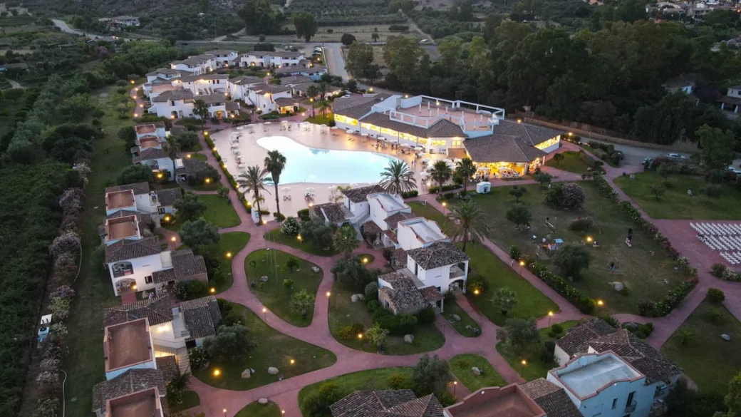 Vista aerea serale del resort con piscina illuminata e giardini con vialetti
