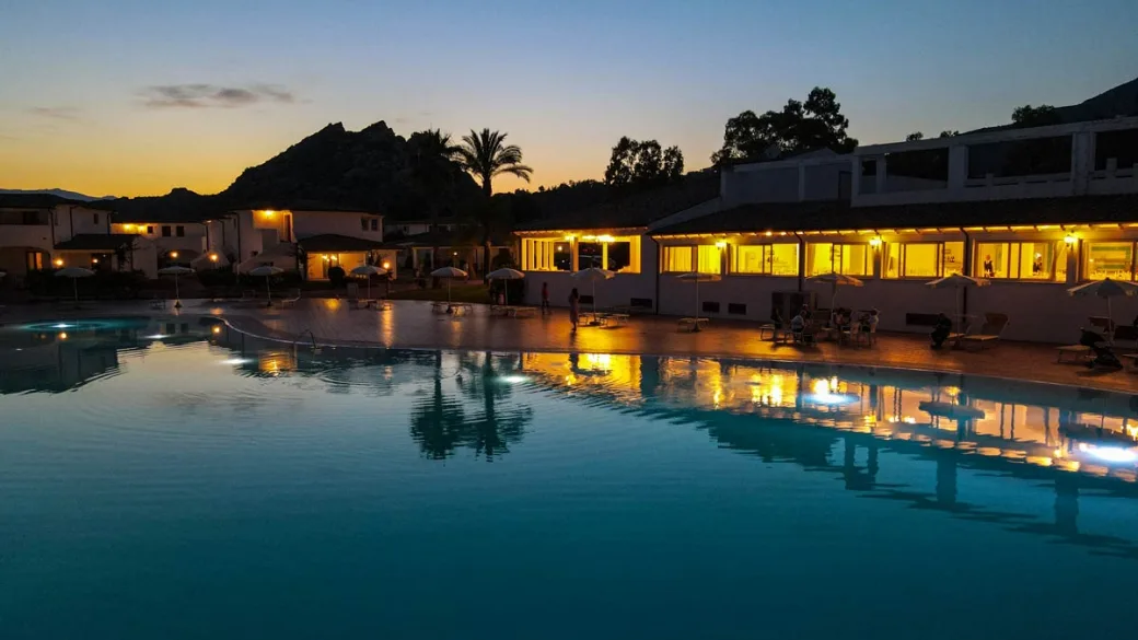 Piscina del resort al crepuscolo con edifici illuminati e palme