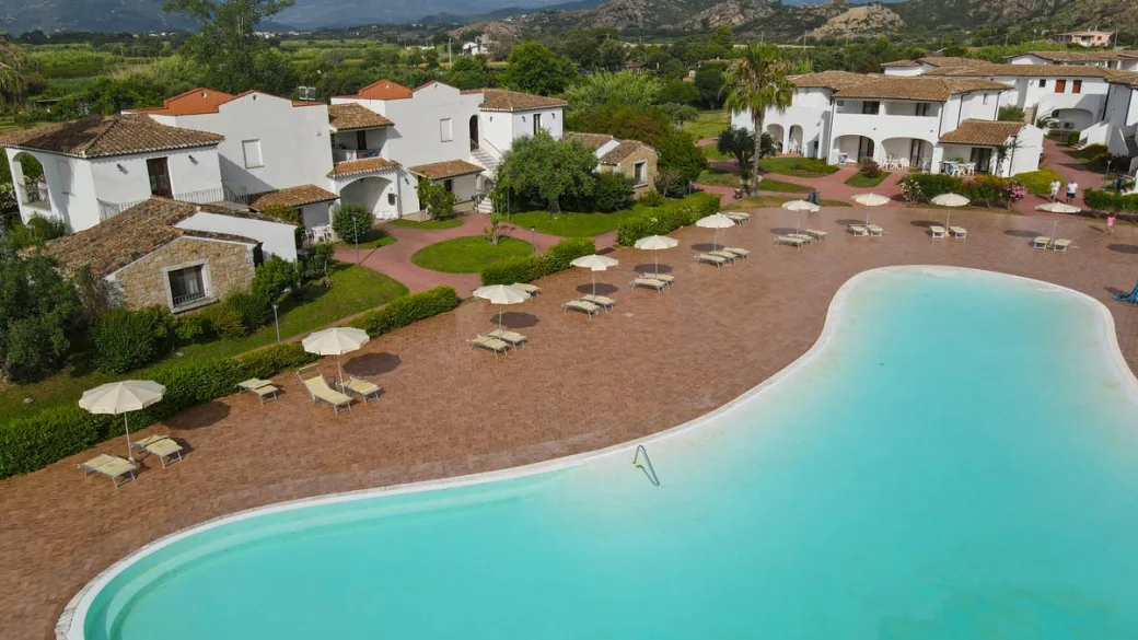 Piscina del resort con ombrelloni, lettini ed edifici bianchi in stile mediterraneo