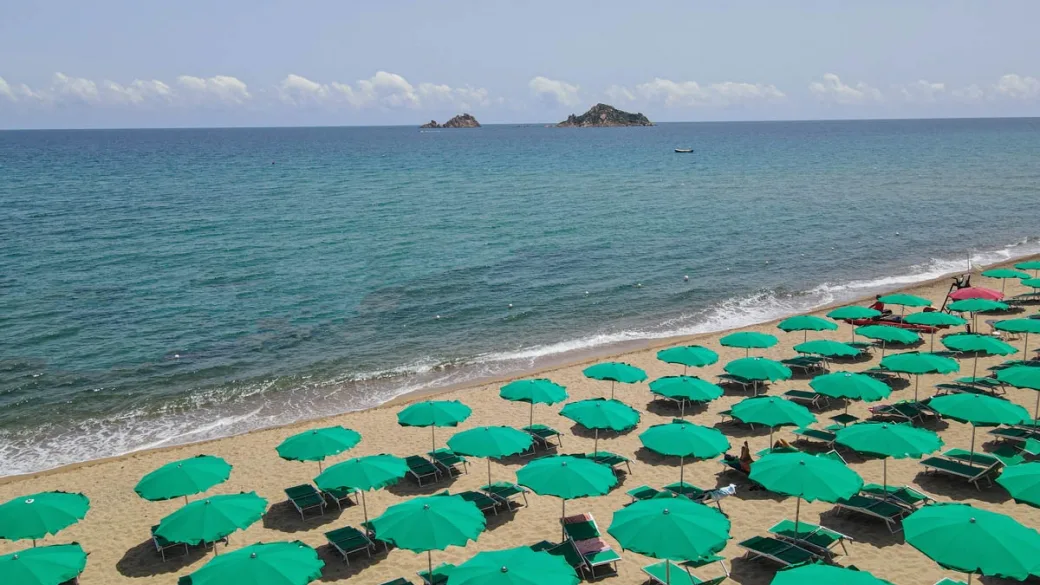Spiaggia con ombrelloni verdi e vista sul mare con isolotti all'orizzonte