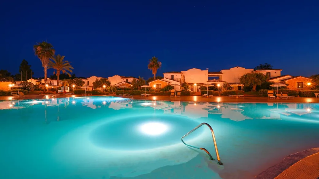 Piscina del resort illuminata di sera con edifici e palme sullo sfondo