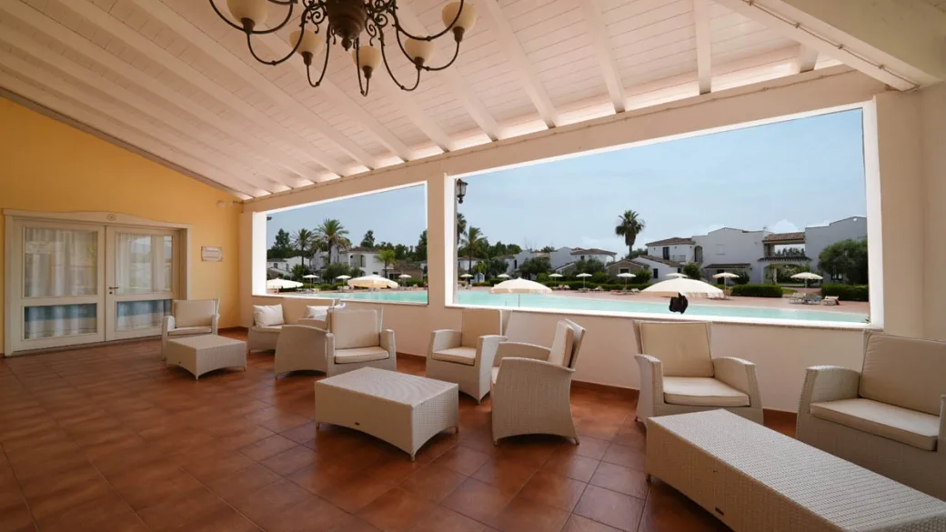 Area lounge coperta con poltrone in vimini e vista sulla piscina