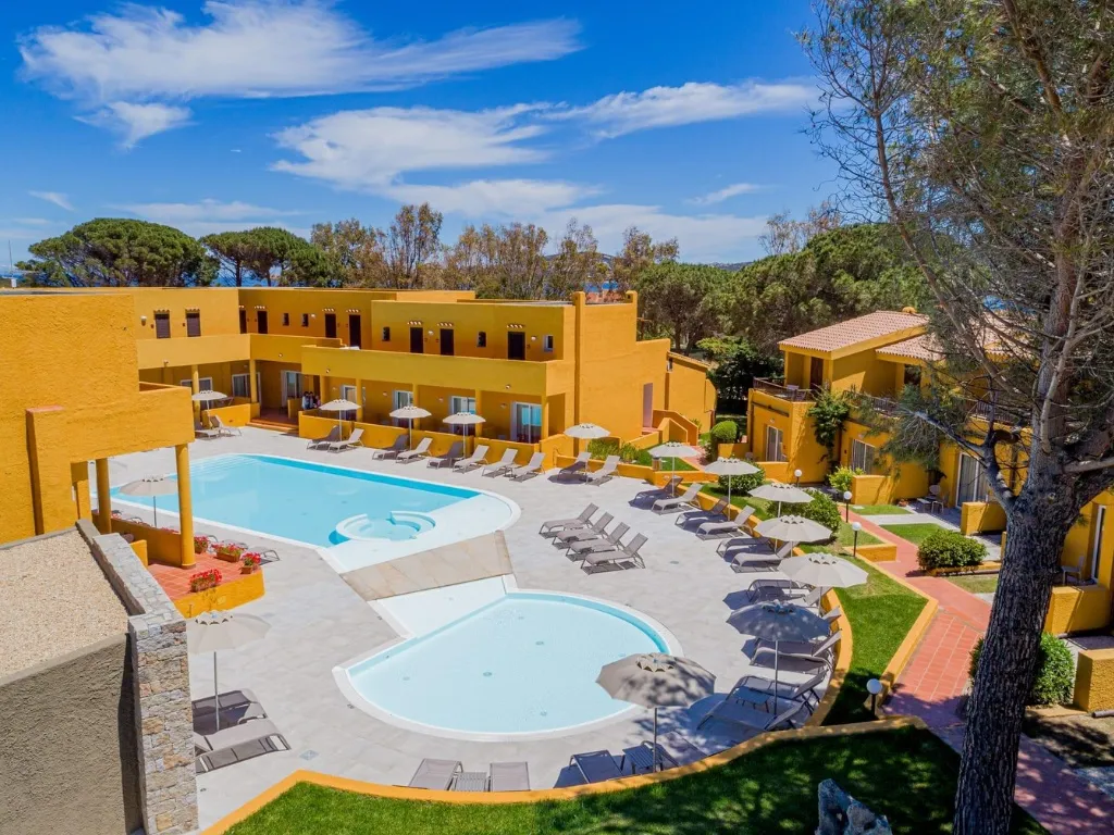 Piscine del resort con lettini e ombrelloni circondate da edifici gialli