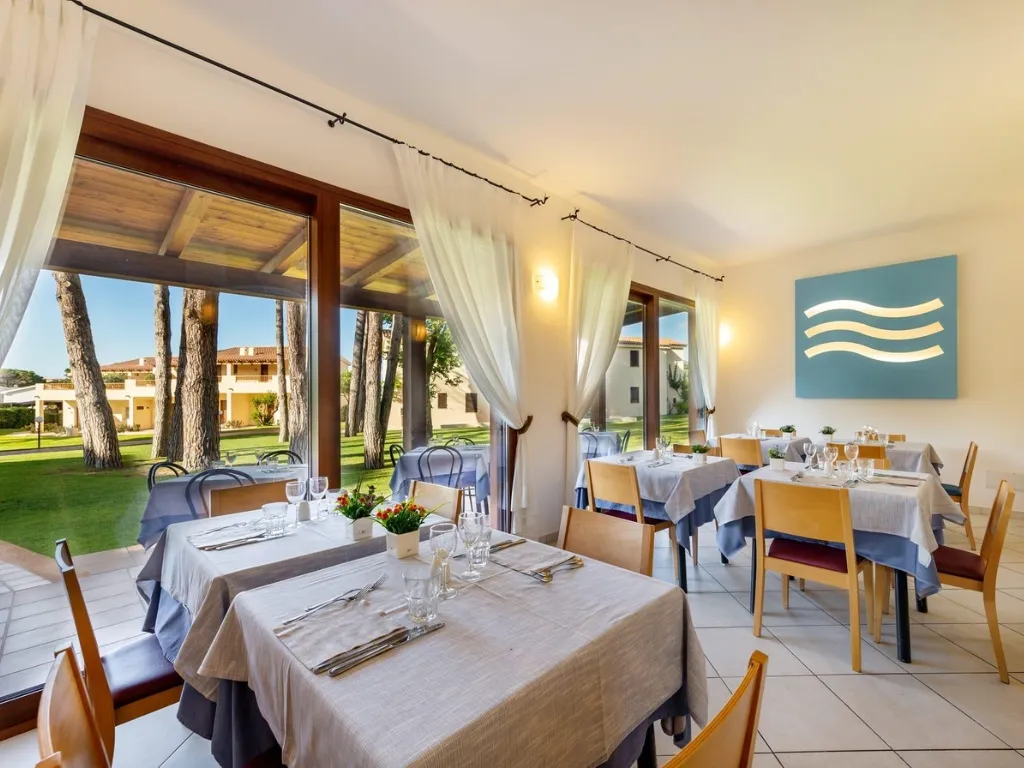 Ristorante con tavoli apparecchiati e grandi vetrate sul verde