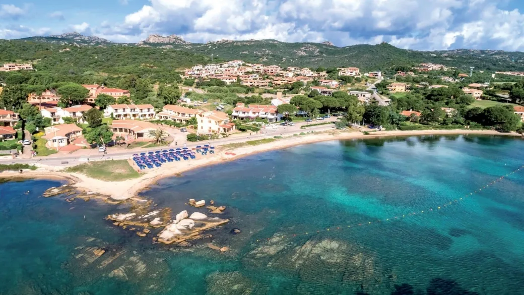 Panorama aereo della baia con spiaggia, ombrelloni e colline verdi