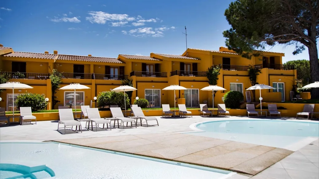 Piscina del resort con lettini e ombrelloni davanti agli edifici gialli