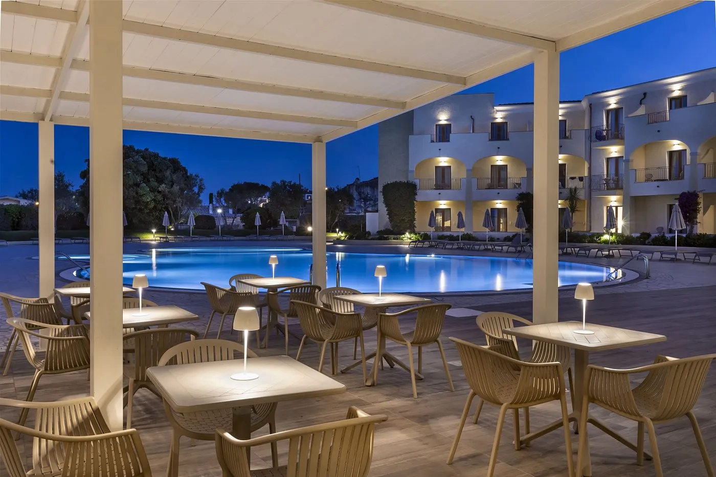 Terrazza con tavoli illuminati e piscina al crepuscolo
