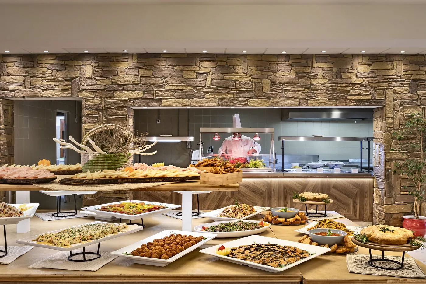 Buffet con antipasti, salumi e cuoco che cucina dietro il bancone
