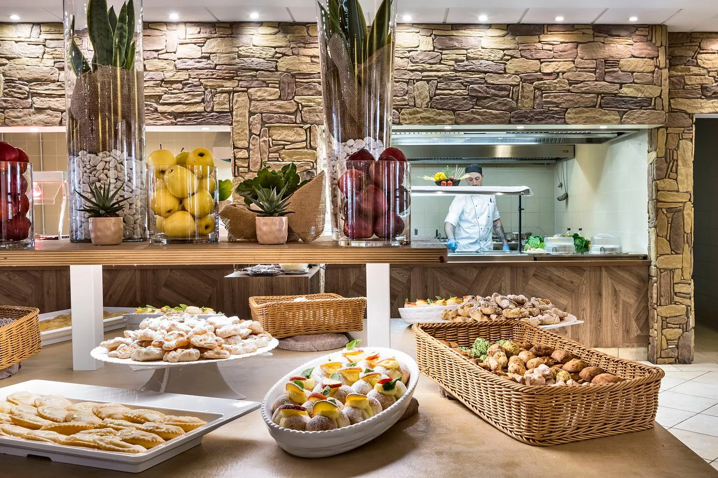 Buffet di dolci e frutta con cuoco al lavoro in cucina a vista
