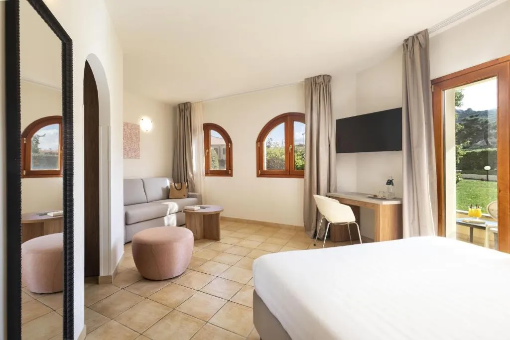 Junior suite con zona soggiorno, divano e finestre ad arco sul giardino