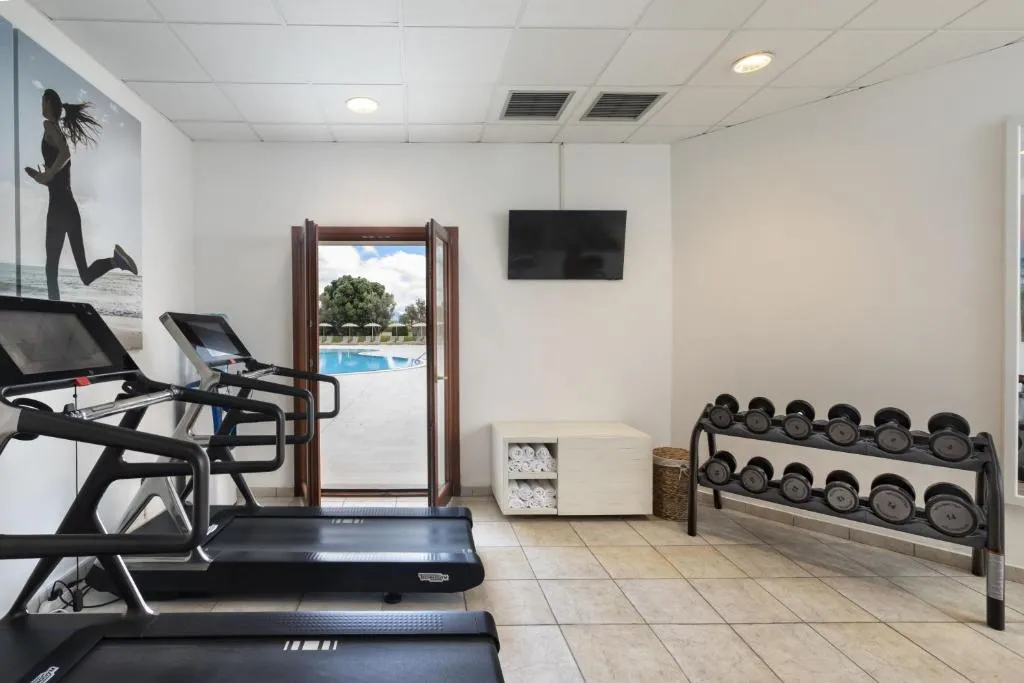 Sala fitness con attrezzi cardio e manubri e porta aperta sulla piscina