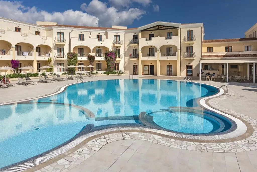 Grande piscina sagomata con lettini e facciata dell'hotel illuminata dal sole