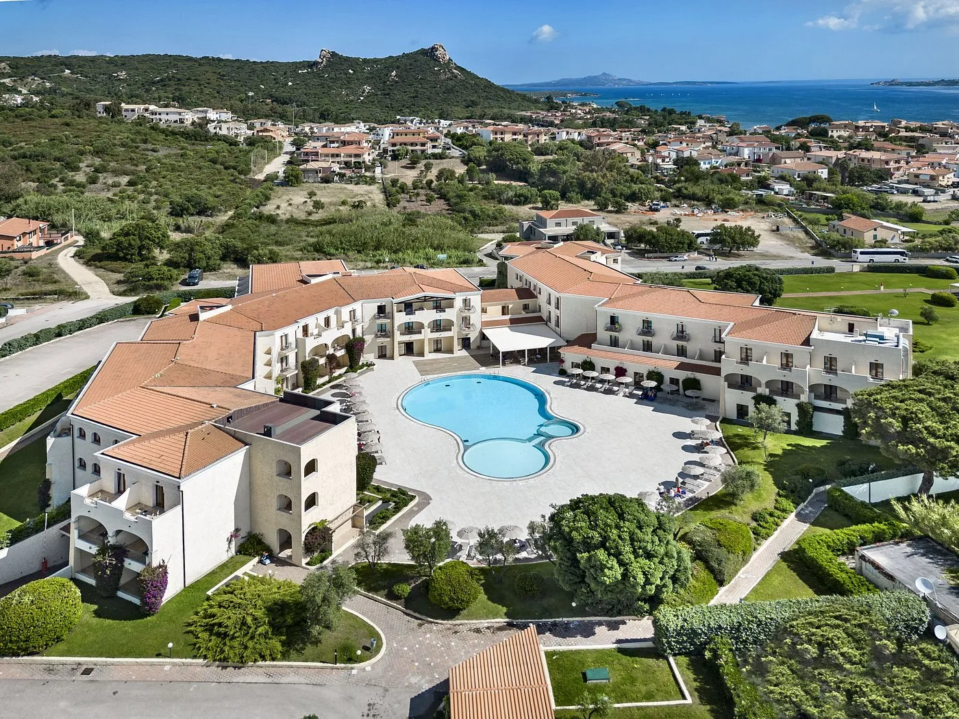 Veduta aerea del resort con piscina centrale e colline verdi verso il mare