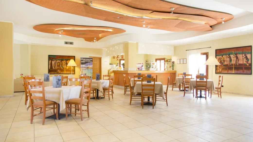Sala da pranzo luminosa con tavoli, bancone bar e dipinti alle pareti