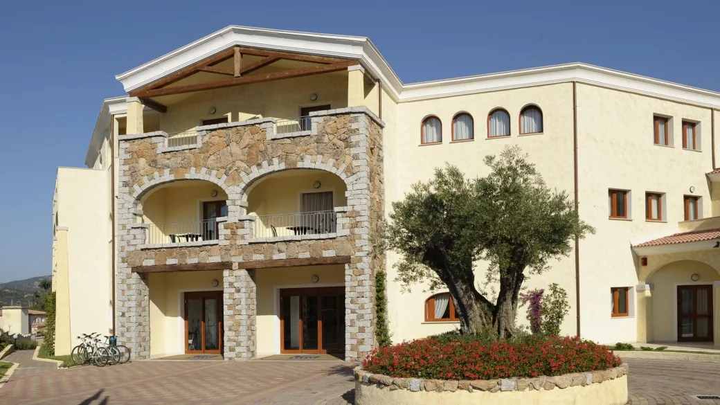 Facciata in pietra dell'hotel con ulivo e aiuola fiorita nel cortile