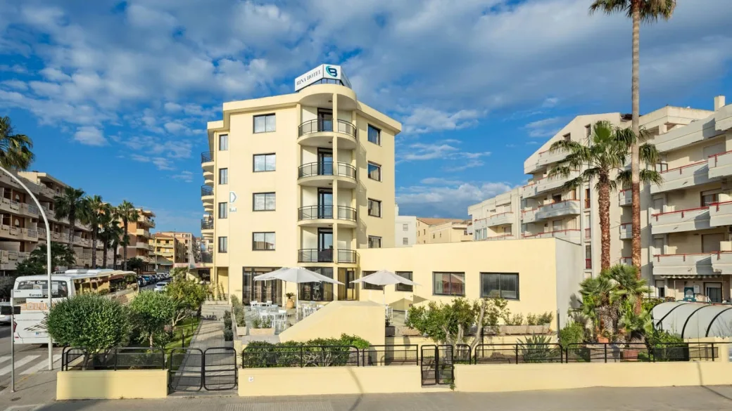 Facciata frontale del Rina Hotel con insegna, terrazza esterna e palme in giornata soleggiata