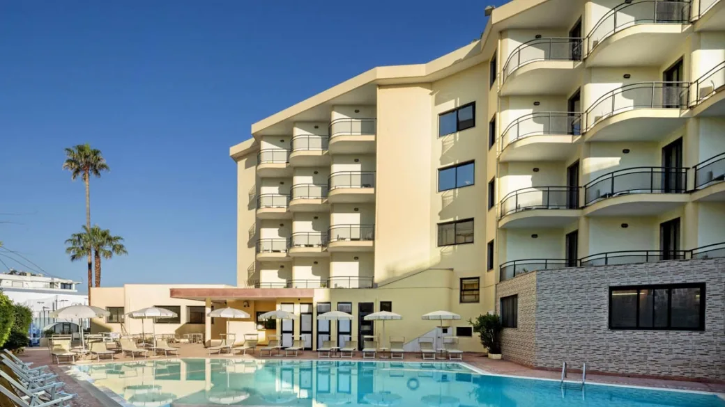 Esterno dell'hotel con piscina, lettini e ombrelloni vicino all'edificio con balconi