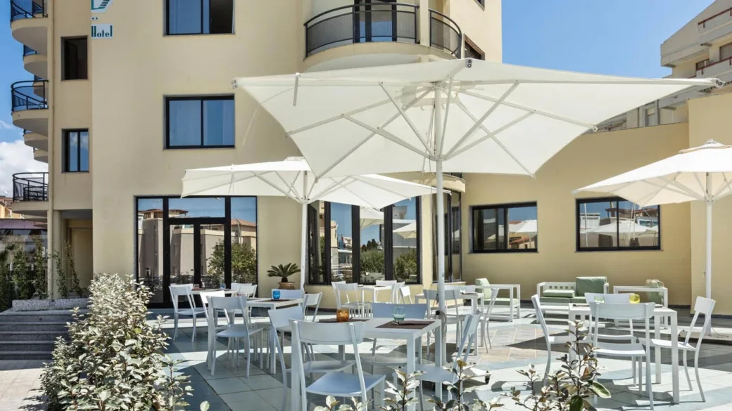 Terrazza esterna dell'hotel con tavoli, sedie bianche e grandi ombrelloni