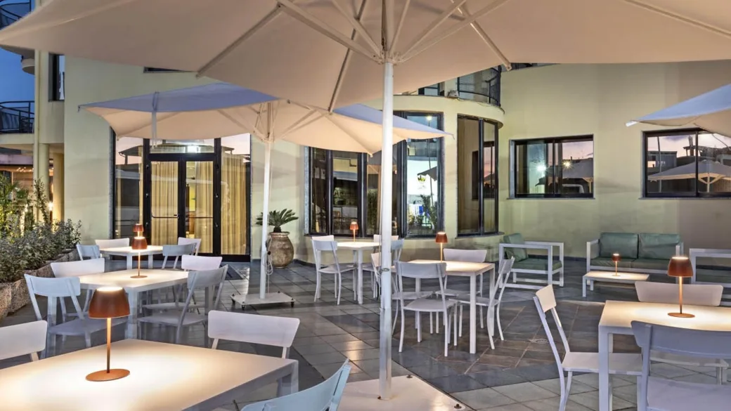 Terrazza ristorante serale con tavoli bianchi, lampade e ombrelloni illuminati