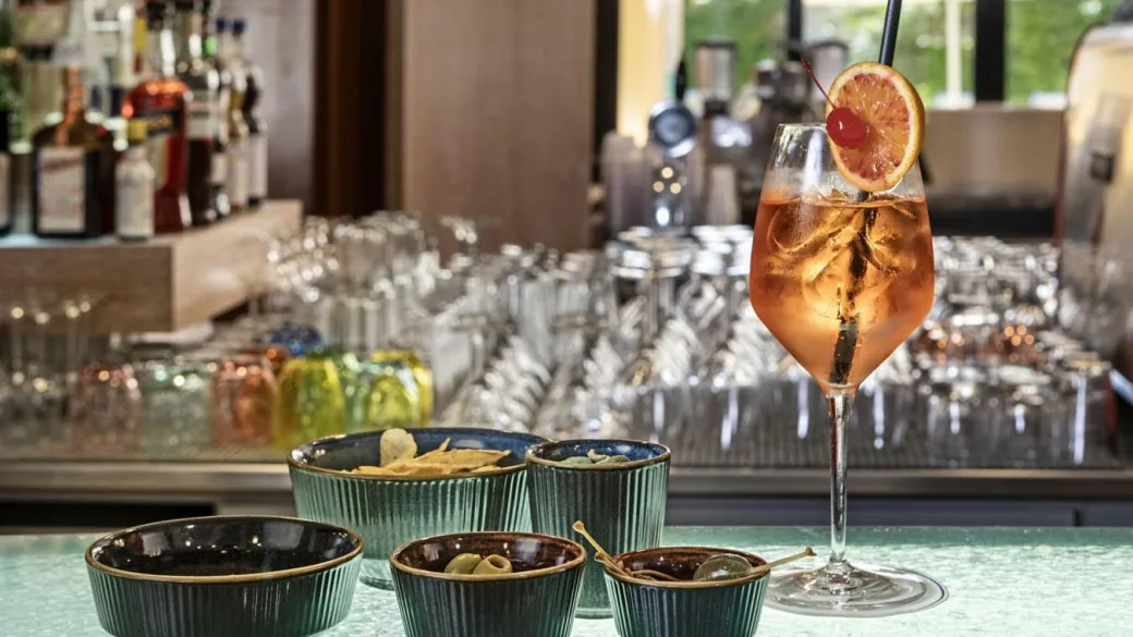 Cocktail con fetta d'arancia e ciotole di snack sul bancone del bar
