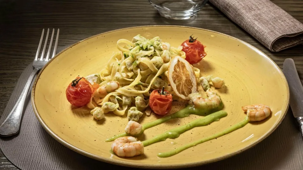 Piatto di tagliatelle con gamberi, pomodorini e salsa verde su piatto giallo
