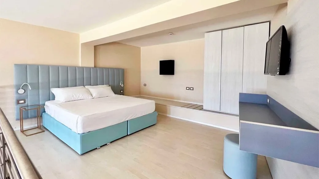 Camera spaziosa con letto matrimoniale azzurro, armadio bianco e TV a parete
