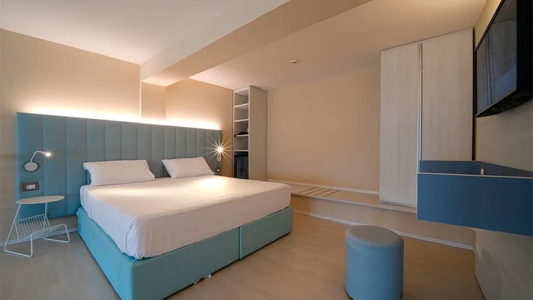 Camera luminosa con letto matrimoniale azzurro, illuminazione soffusa e TV a parete