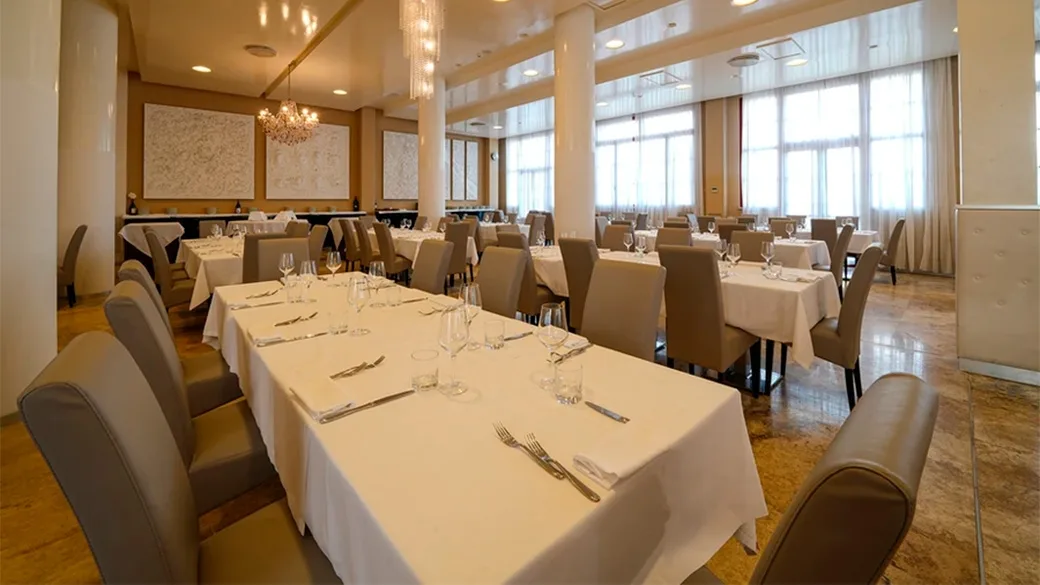Ristorante con tavoli dalle tovaglie bianche apparecchiati, ampie finestre e lampadari
