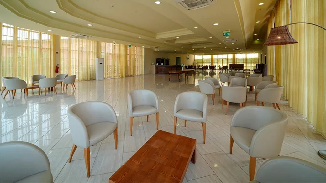 Ampia sala comune luminosa con poltrone bianche, tavolini e grandi tende