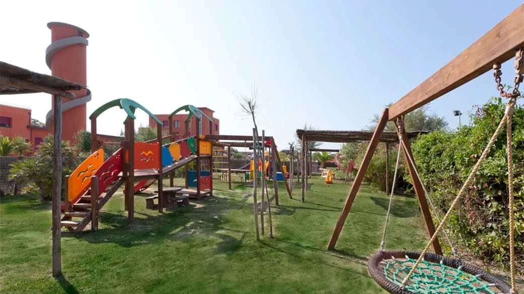 Parco giochi per bambini con scivoli, altalene e strutture in legno nel giardino dell'hotel