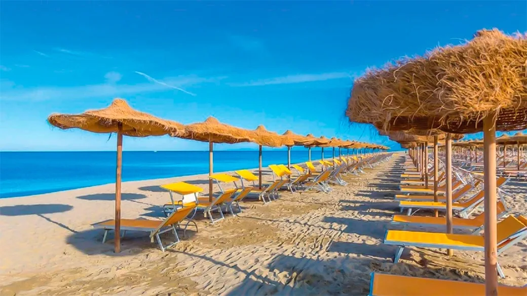 Spiaggia attrezzata con ombrelloni in paglia e lettini gialli affacciati sul mare azzurro