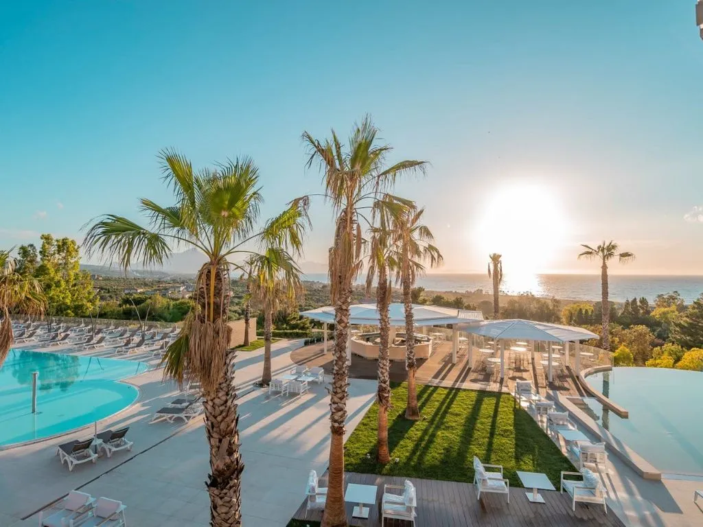 Piscina con palme e lettini bianchi affacciata sul mare al tramonto