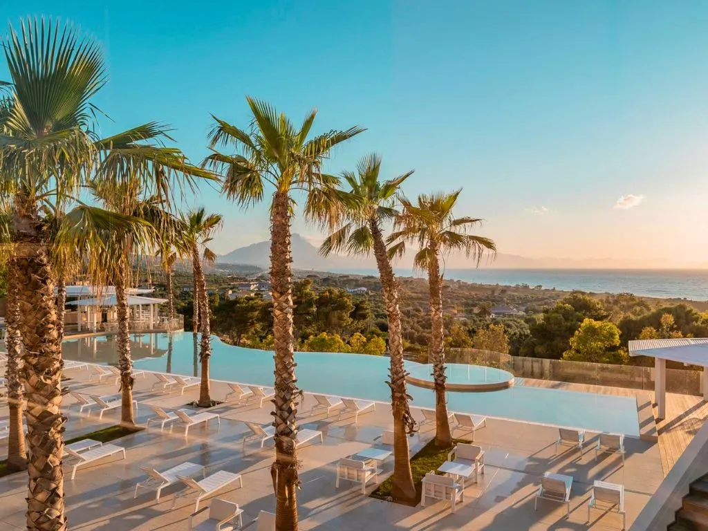 Piscina a sfioro con palme e vista panoramica sul mare al tramonto