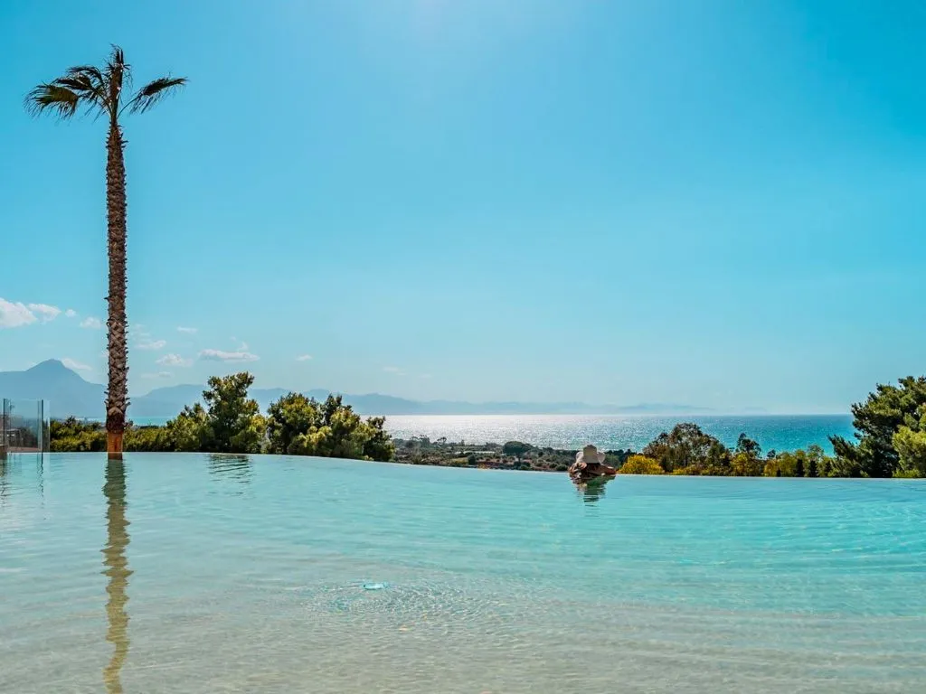Piscina a sfioro con palma e vista sul mare e montagne