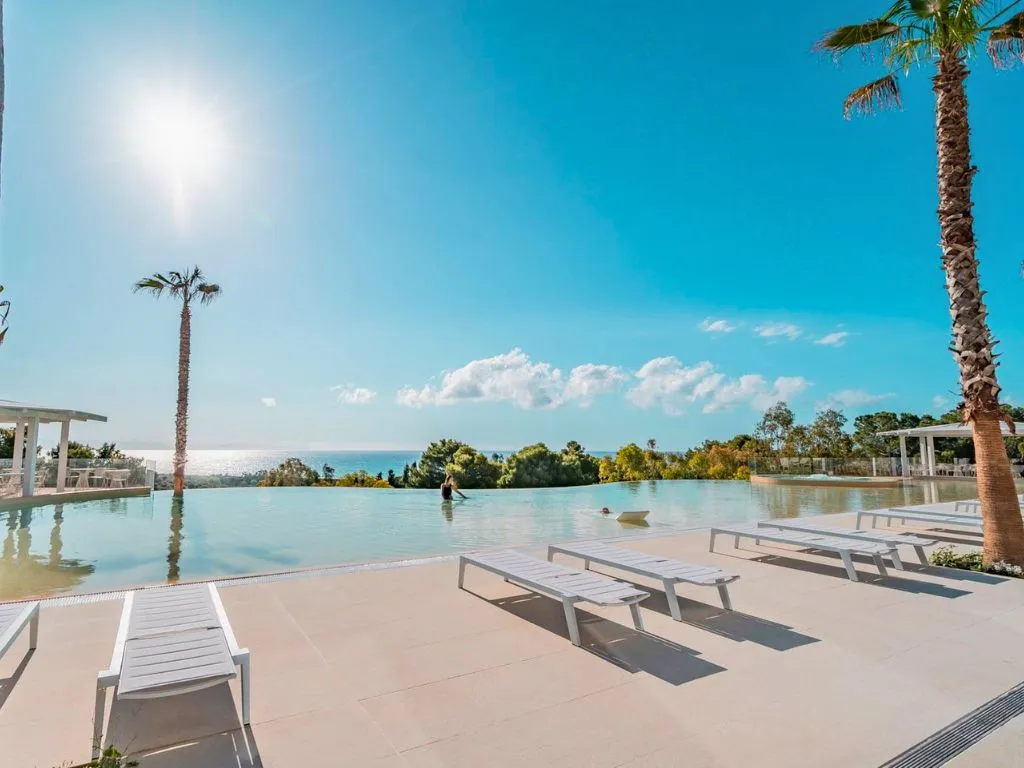 Piscina a sfioro con lettini bianchi e vista sul mare sotto il sole