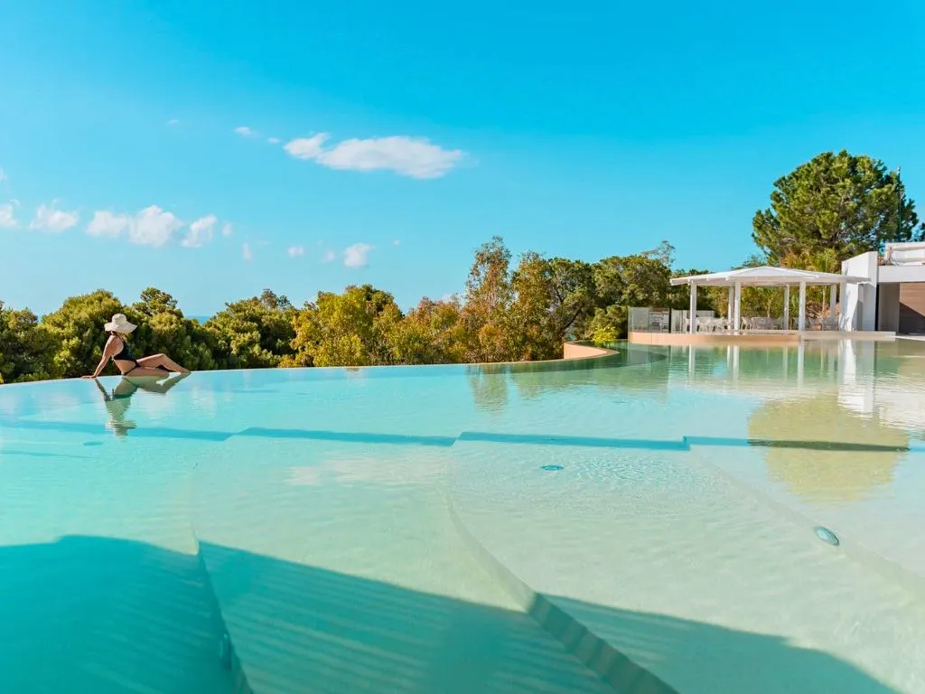 Piscina a sfioro con ospite immersa e vista sulla vegetazione e mare