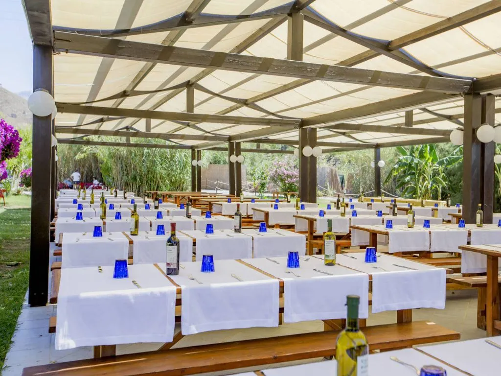 Area pranzo all'aperto sotto pergola con tavoli apparecchiati e vegetazione