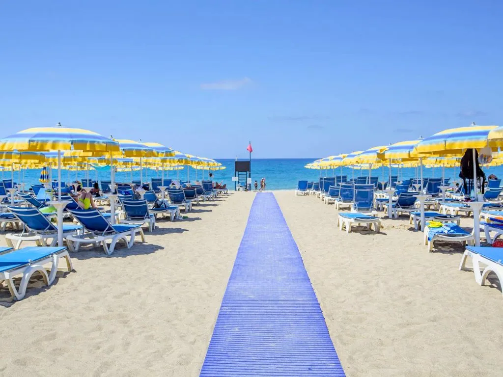 Spiaggia attrezzata con passerella, ombrelloni gialli e blu verso il mare