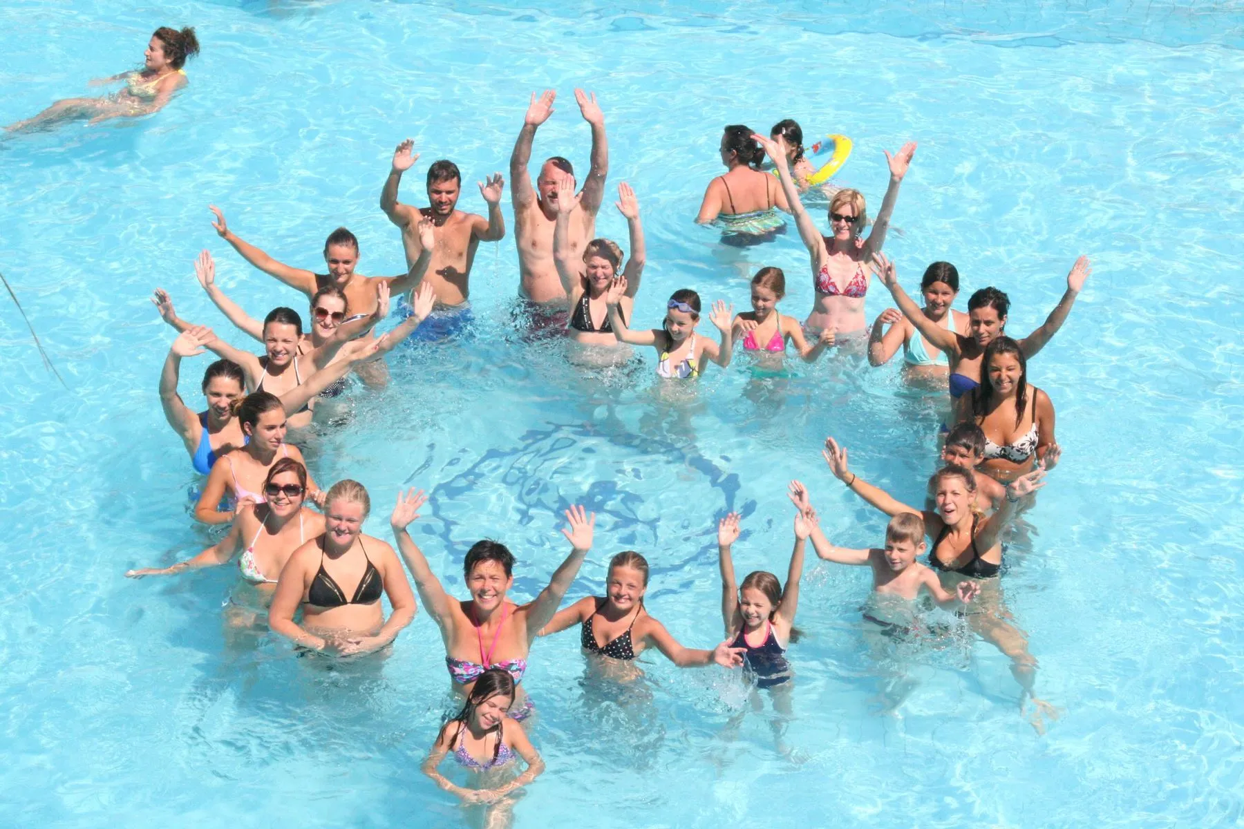 Gruppo di ospiti sorridenti in piscina che salutano con le mani alzate