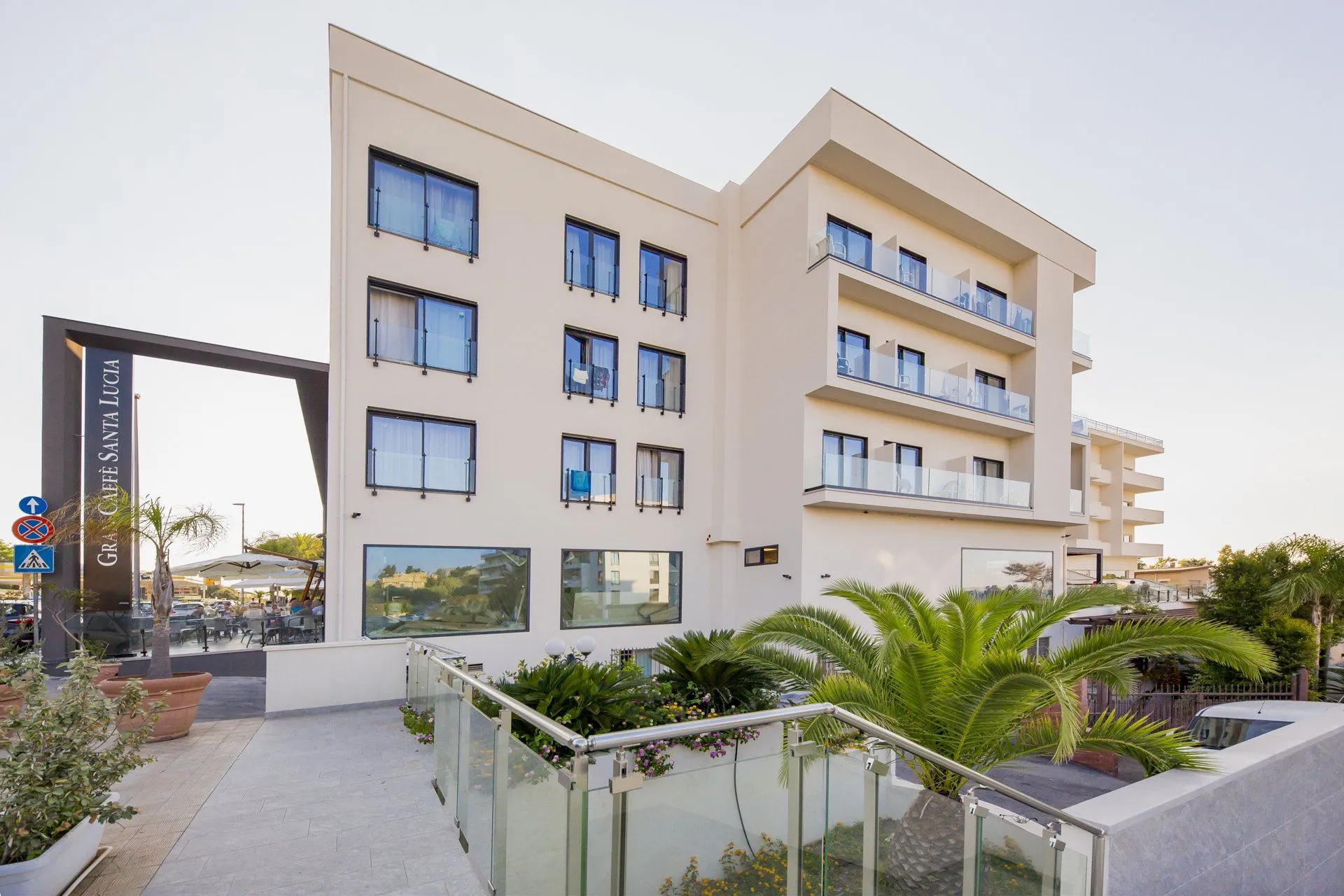Facciata moderna dell'hotel con balconi, palme e caffetteria al piano terra