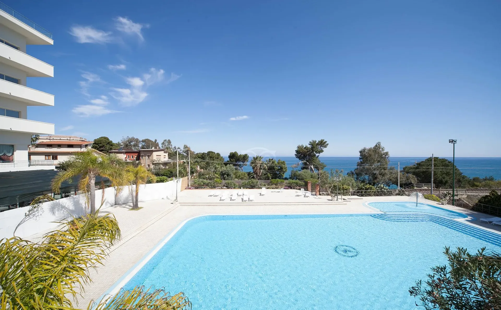 Piscina esterna con palme e vista panoramica sul mare in giornata soleggiata