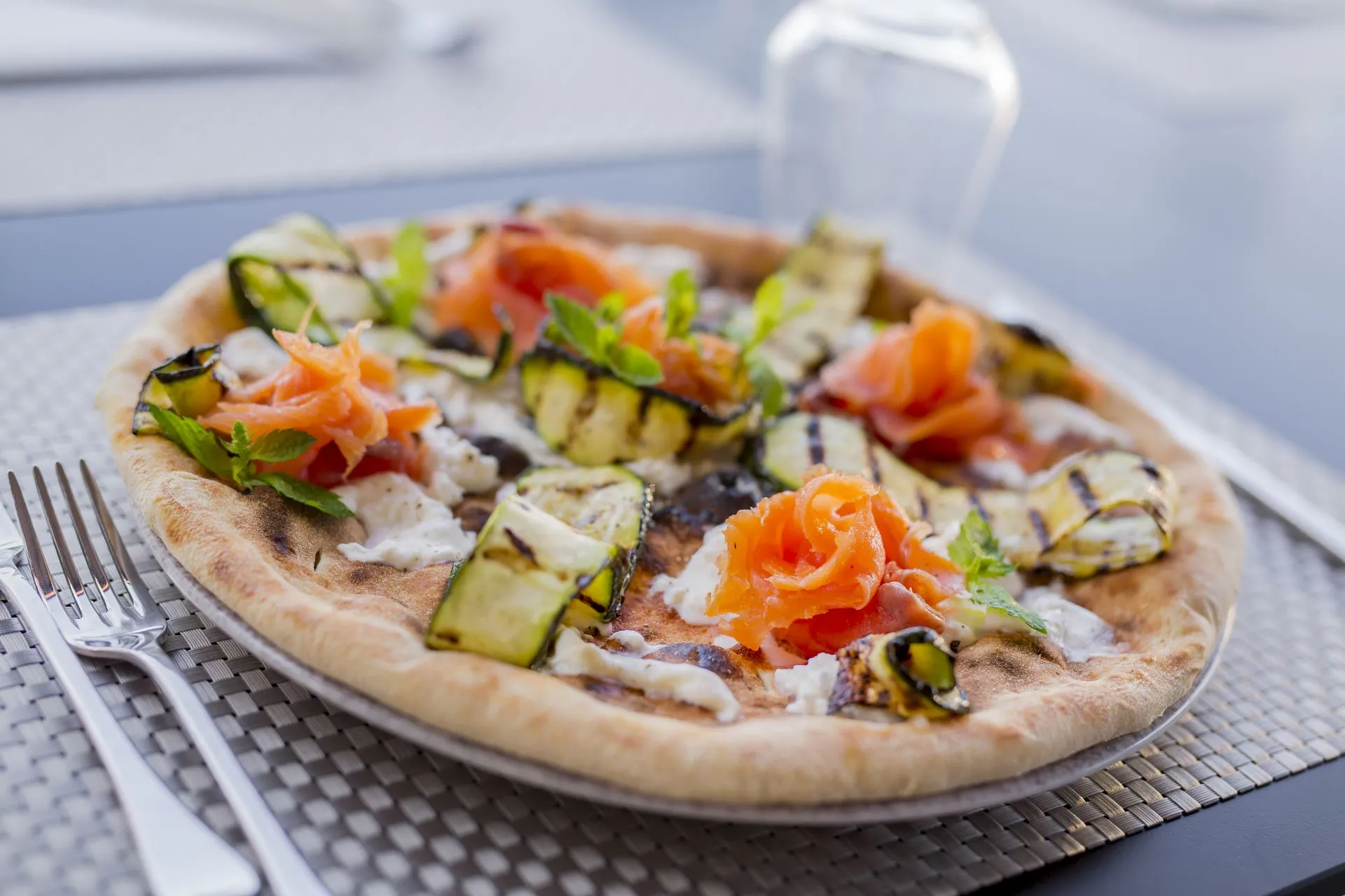 Pizza gourmet con zucchine grigliate, salmone e menta servita al tavolo