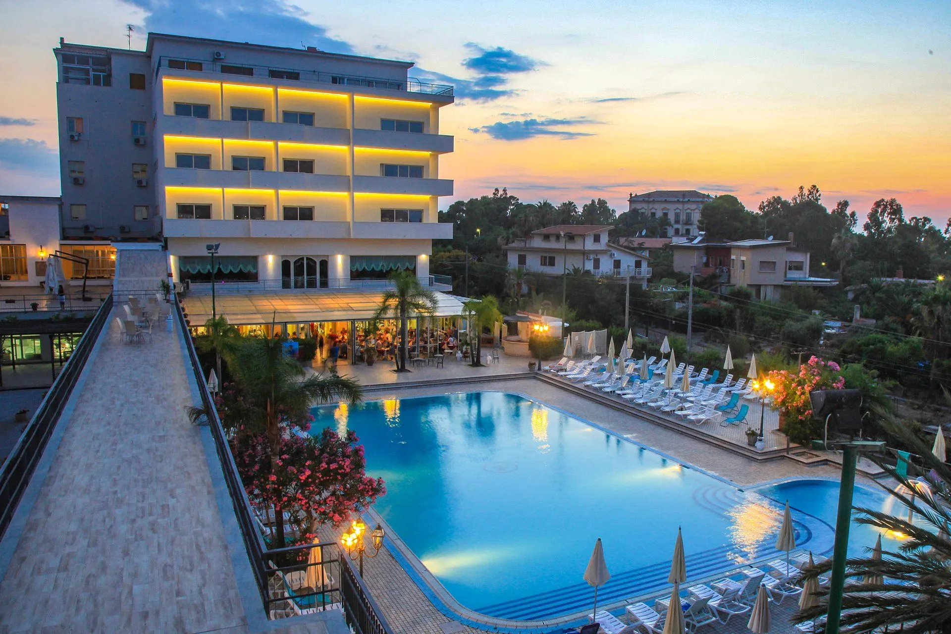 Piscina dell'hotel al tramonto con lettini illuminati e ristorante affollato sullo sfondo