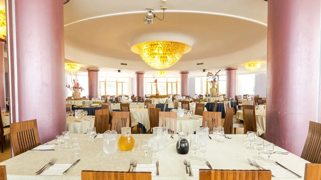 Sala ristorante interna con tavoli apparecchiati, colonne rosa e lampadari dorati