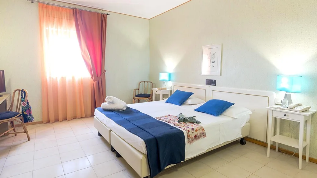 Camera matrimoniale luminosa con letto, dettagli blu e tende rosa alla finestra