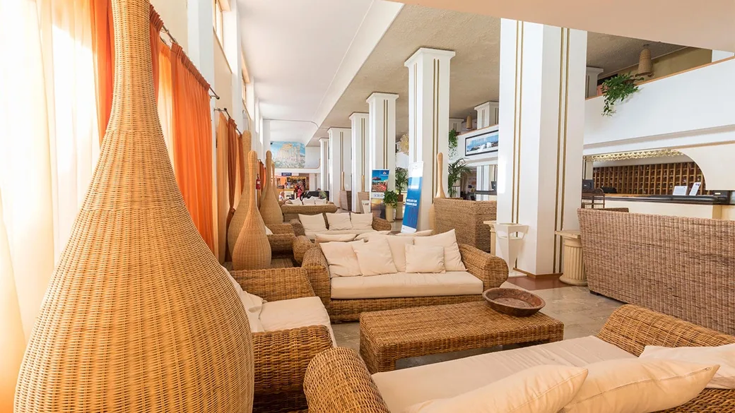 Hall dell'hotel con divani e poltrone in vimini e reception sullo sfondo