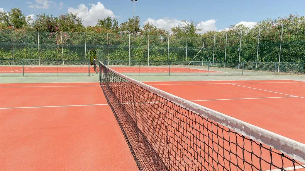 Campi da tennis in terra rossa con rete e recinzione immersi nel verde