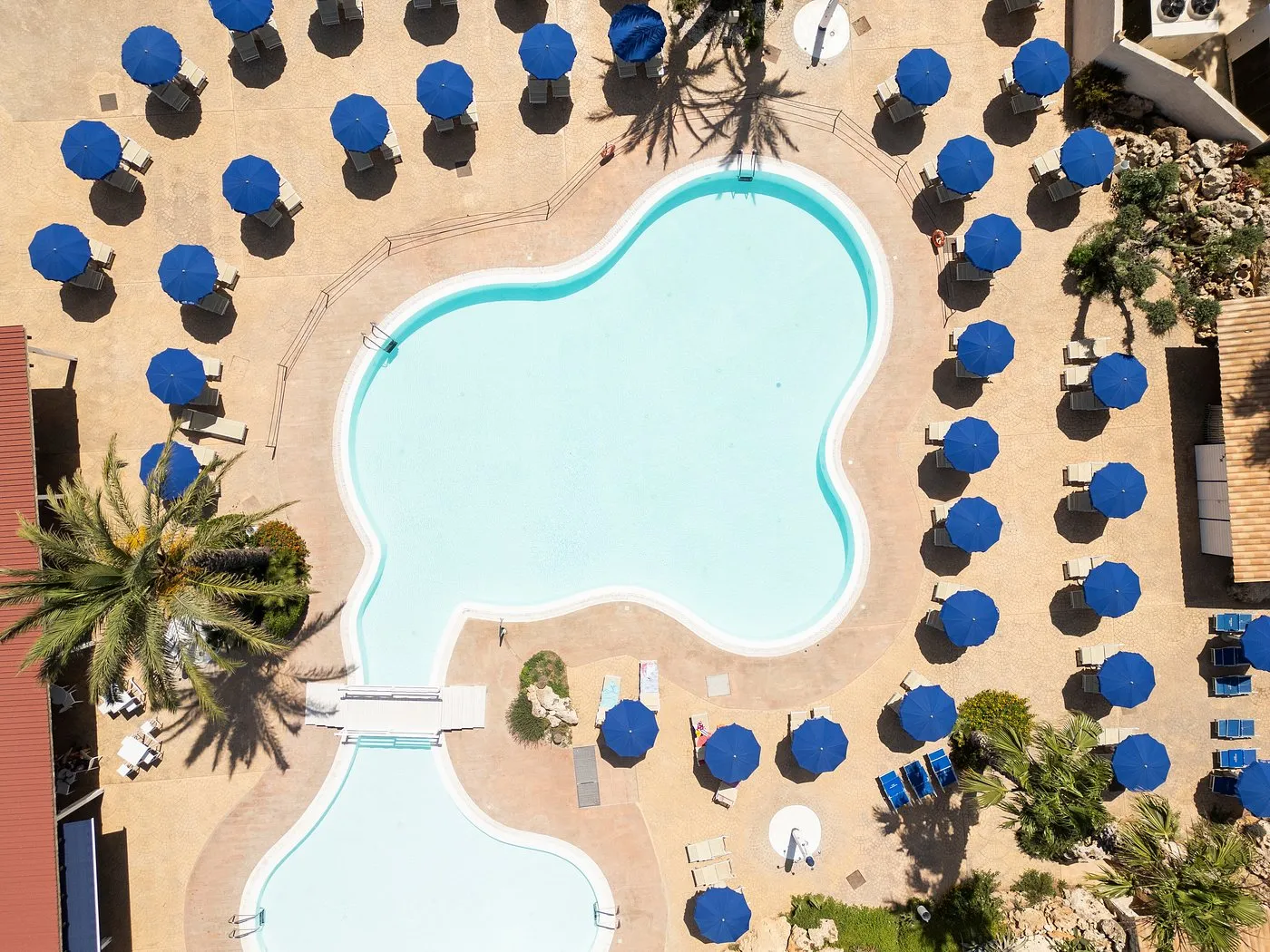 Vista dall'alto della piscina a forma libera circondata da ombrelloni blu e palme