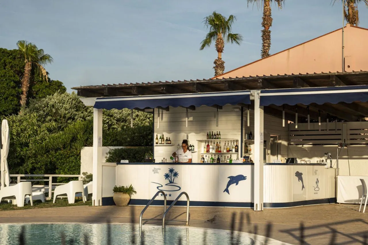 Bar a bordo piscina in legno bianco con decorazioni di delfini e barista al lavoro