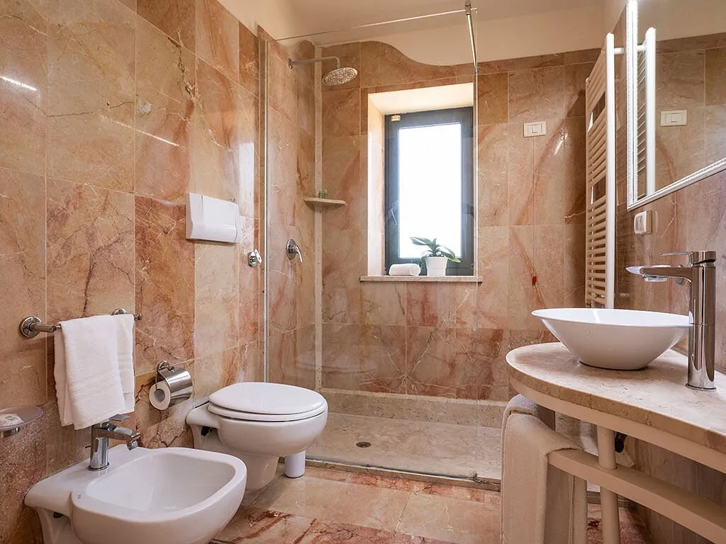 Bagno rivestito in marmo rosato con doccia, bidet, wc e lavabo a bacinella